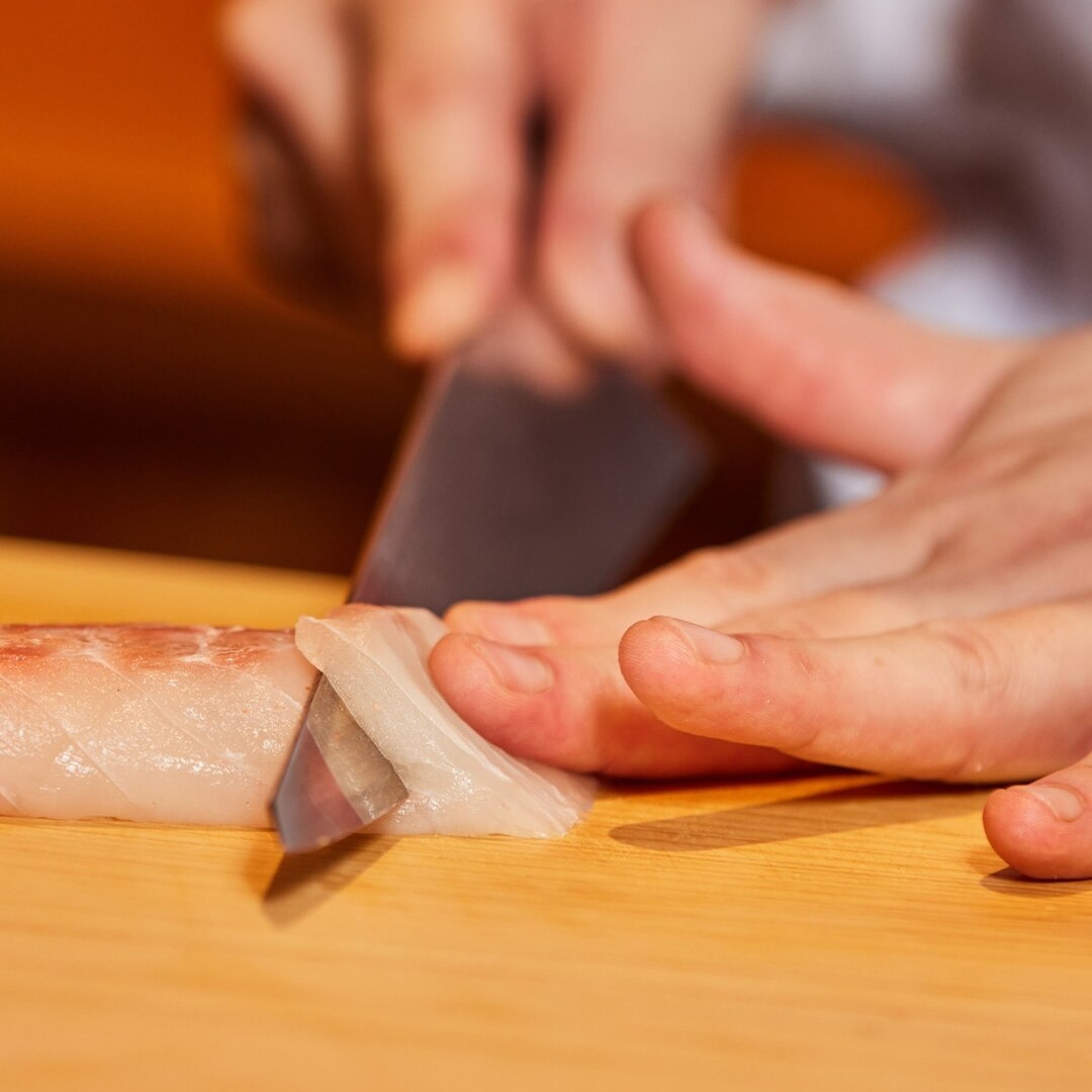 在新加坡 Omakase 餐廳，廚師正切下一片生魚片。